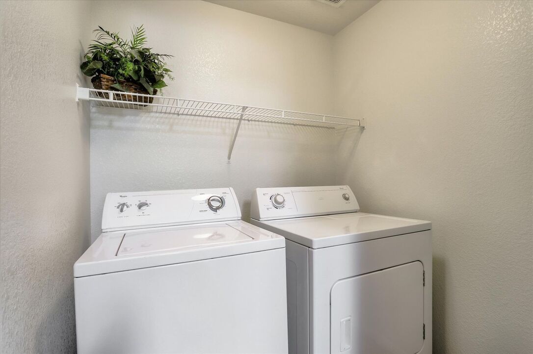 Image of laundry room equipped with full size washer and dryer and overhead shelving.