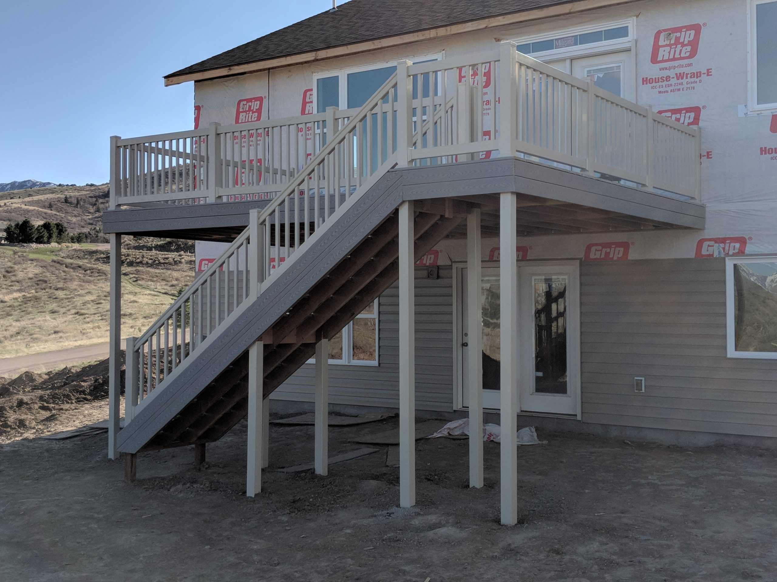 Expand your living space outdoors with a custom second-story deck from DeckPro LLC. This new construction project features durable grey composite decking paired with classic white vinyl railing, providing a safe and stylish elevated retreat with easy access to the yard below via a long staircase.