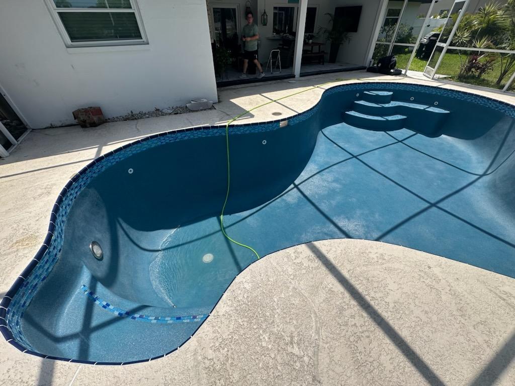 Compact kidney-shaped backyard swimming pool with a light-colored deck and surrounding residential landscaping.