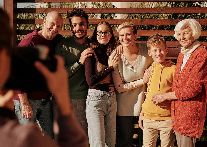 A happy multigenerational family — including grandparents, parents, and children — smiling together in warm sunlight as a family photo is taken, representing comprehensive family wealth management and legacy financial planning across generations.
