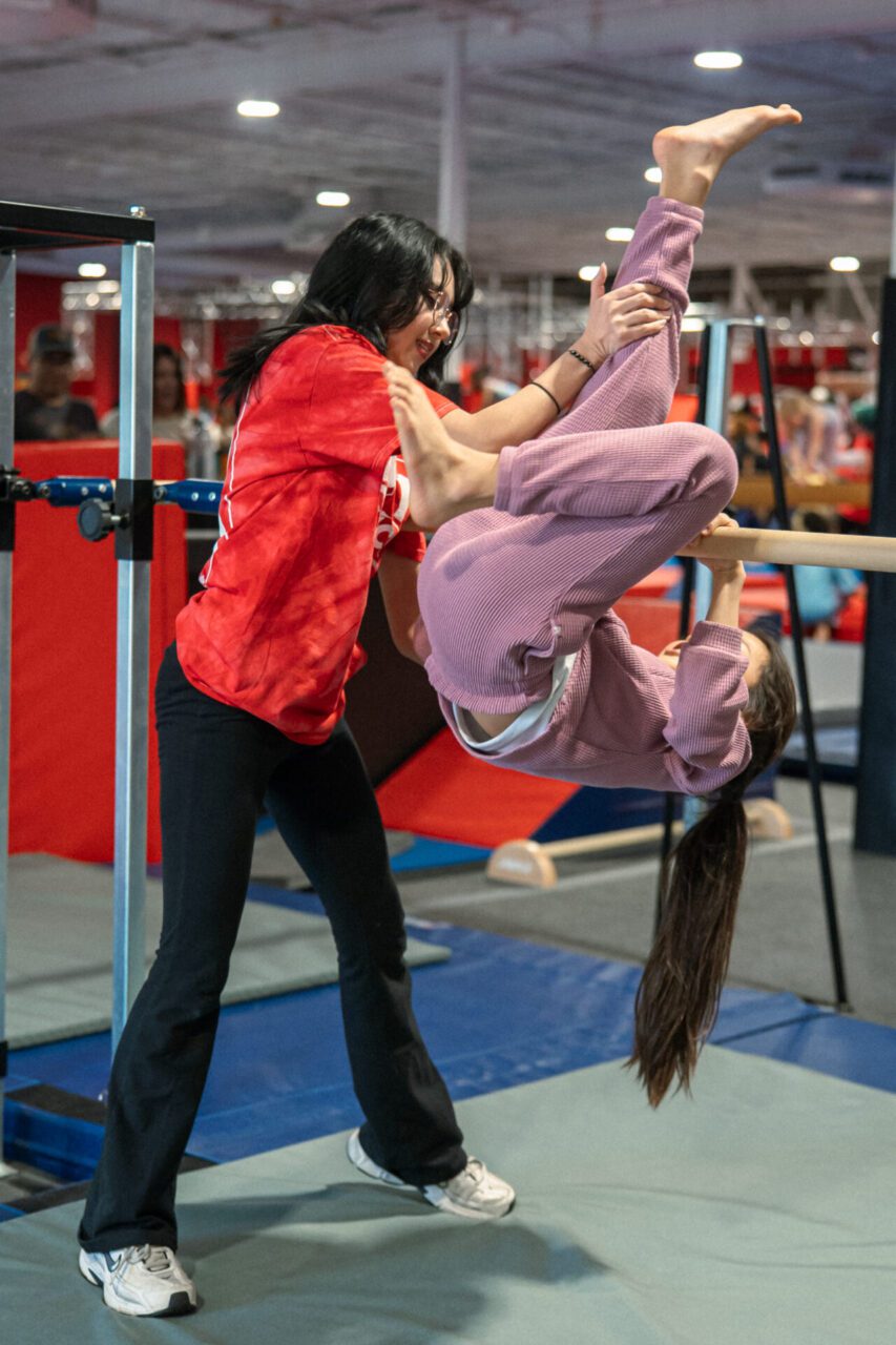 Gymnastics coach helping a young student do a flip on a bar