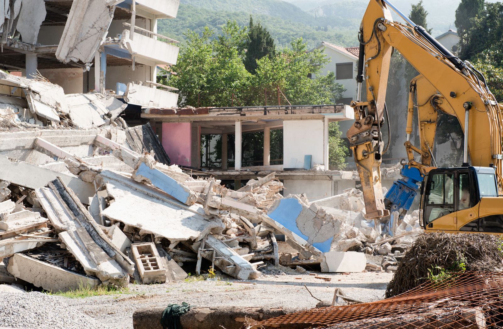 Excavator tearing down large concrete building, surrounded by rubble and debris, demonstrating heavy-duty demolition, structural breakdown, and site clearing for redevelopment or construction preparation.