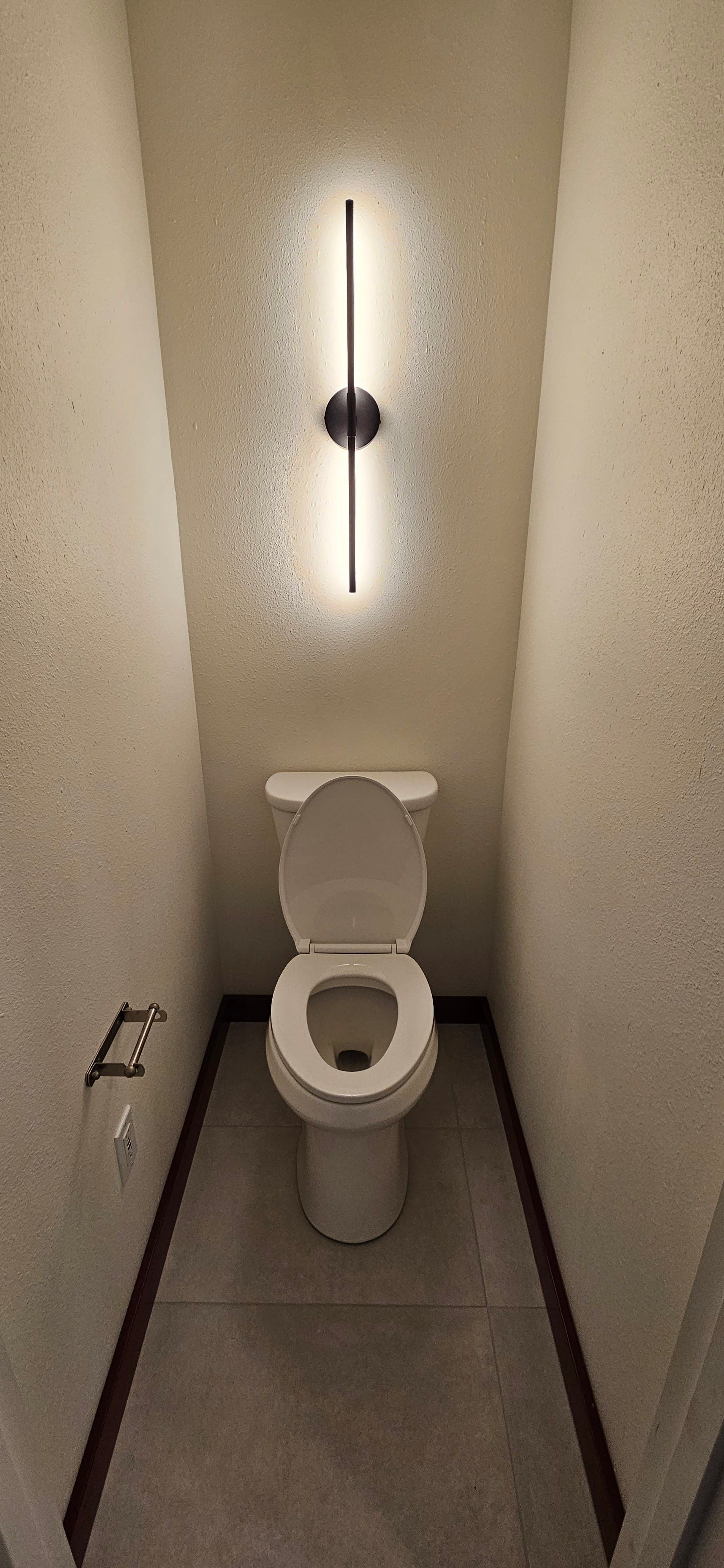 Minimalist bathroom space featuring a white toilet installed between narrow walls, modern vertical w 