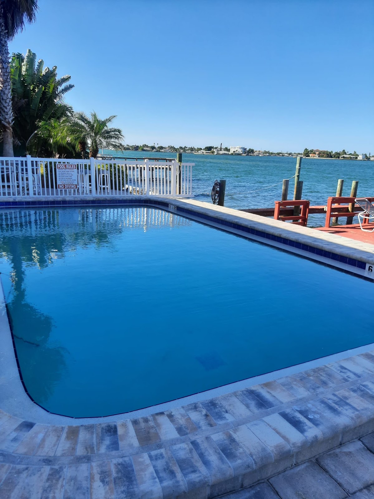 Waterfront backyard swimming pool with deep blue water, light stone coping, outdoor seating, and scenic bay views.