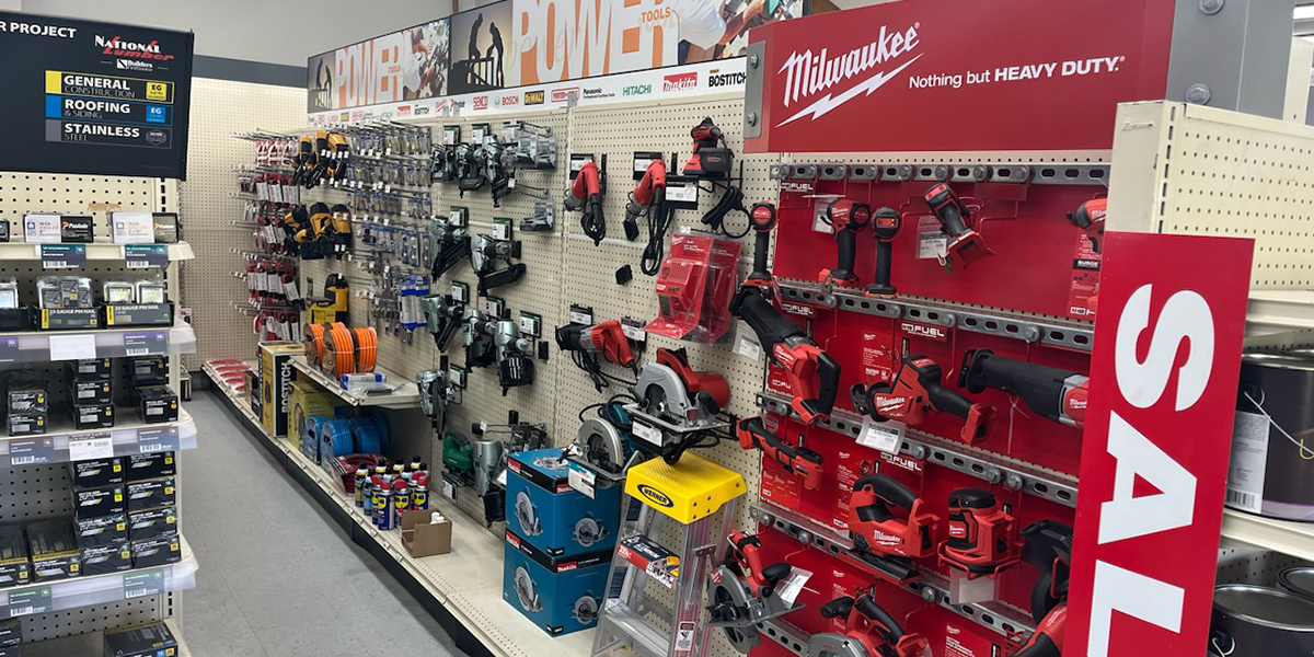 A well-organized display of power tools and equipment at Builders FirstSource, featuring Milwaukee brand tools prominently on shelves, with signage indicating ongoing sales. Various hand tools, drills, and accessories are neatly arranged, catering to both professionals and homeowners.