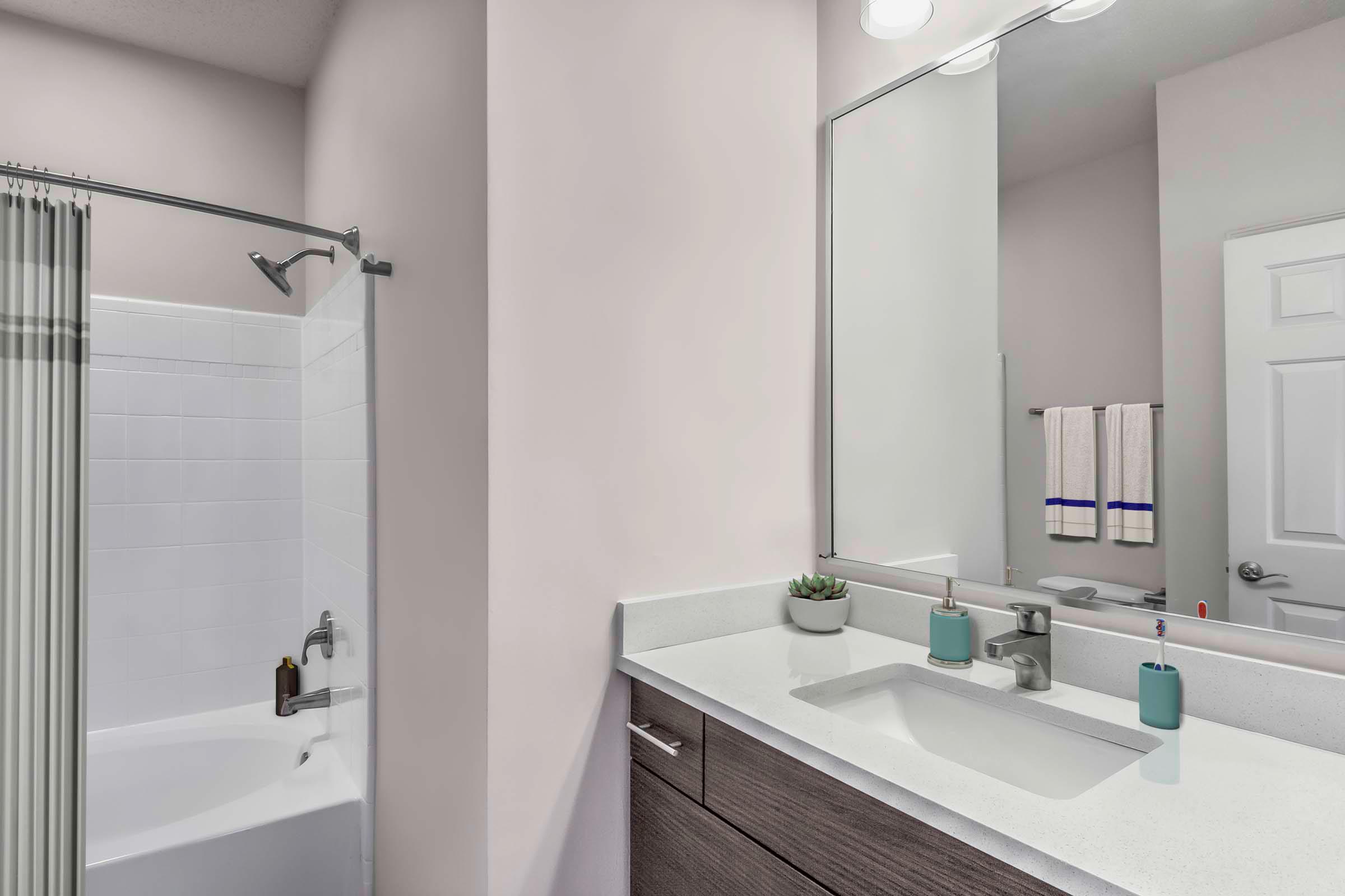 Townhome bathroom with quartz countertop and bathtub with curved shower rod and rainfall showerhead Camden Deerfield Apartments Alpharetta (770)872-6592