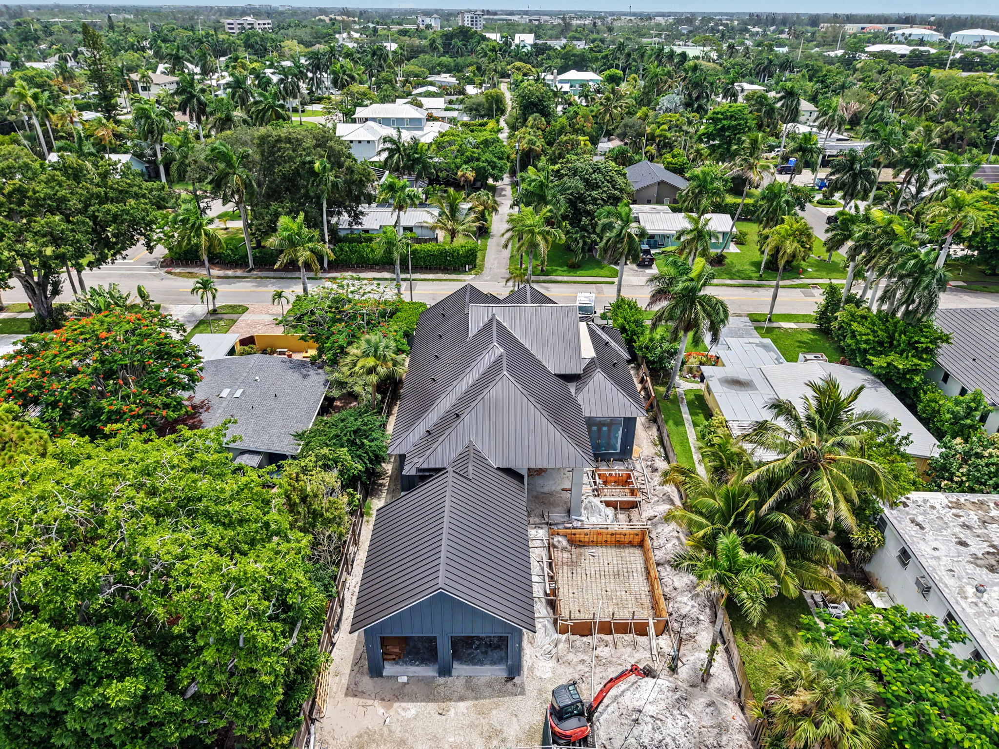Wide drone view of a home under construction showcasing the completed dark metal roof and ongoing wo 