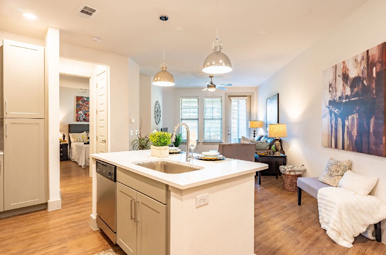 Open floor plan at The Drake Apartments in Midland, TX showing a kitchen island, living area, and be 