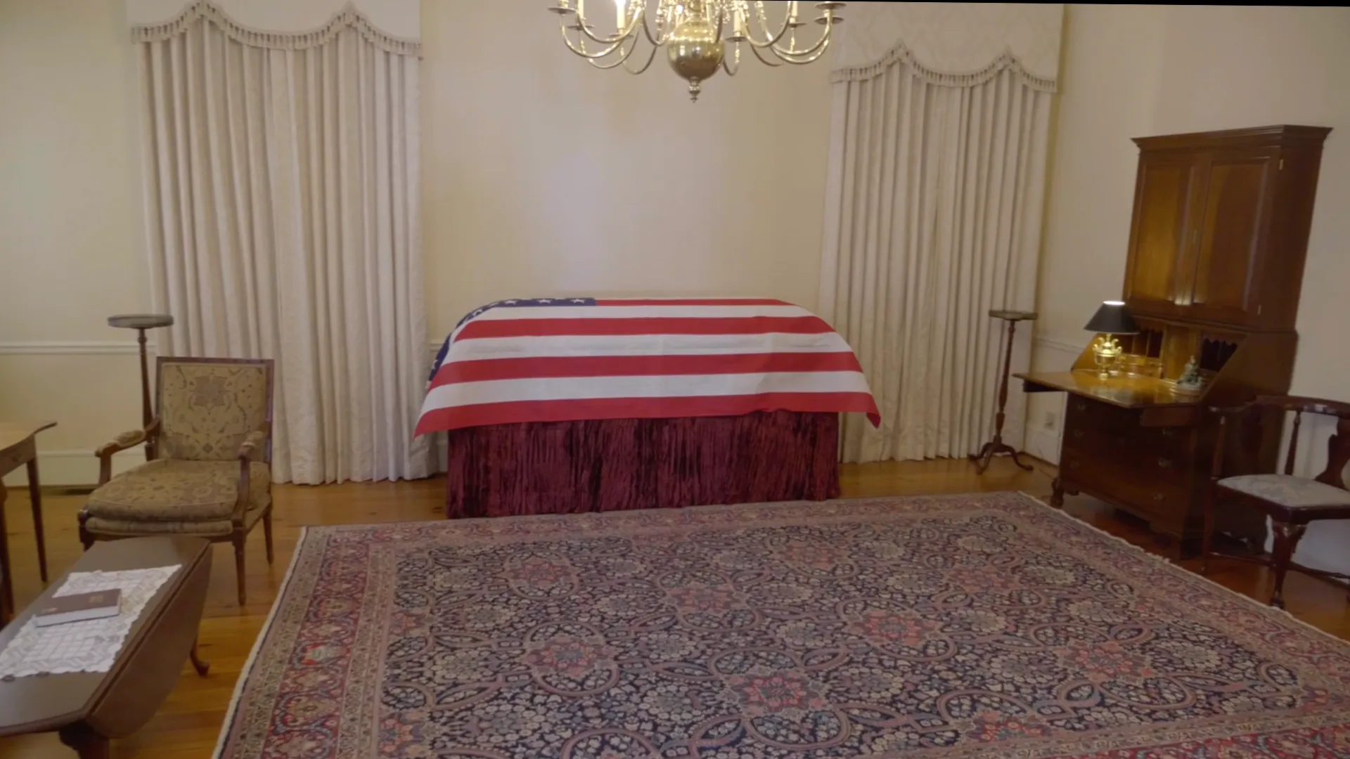 A visitation room at Platt's Augusta set up with a flag-draped casket stand, antique furniture, and  