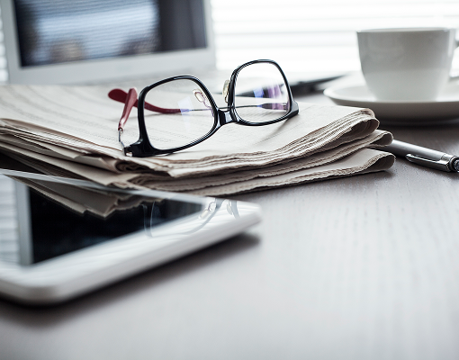 A close up of a folded newspaper with a pair of glasses on top.