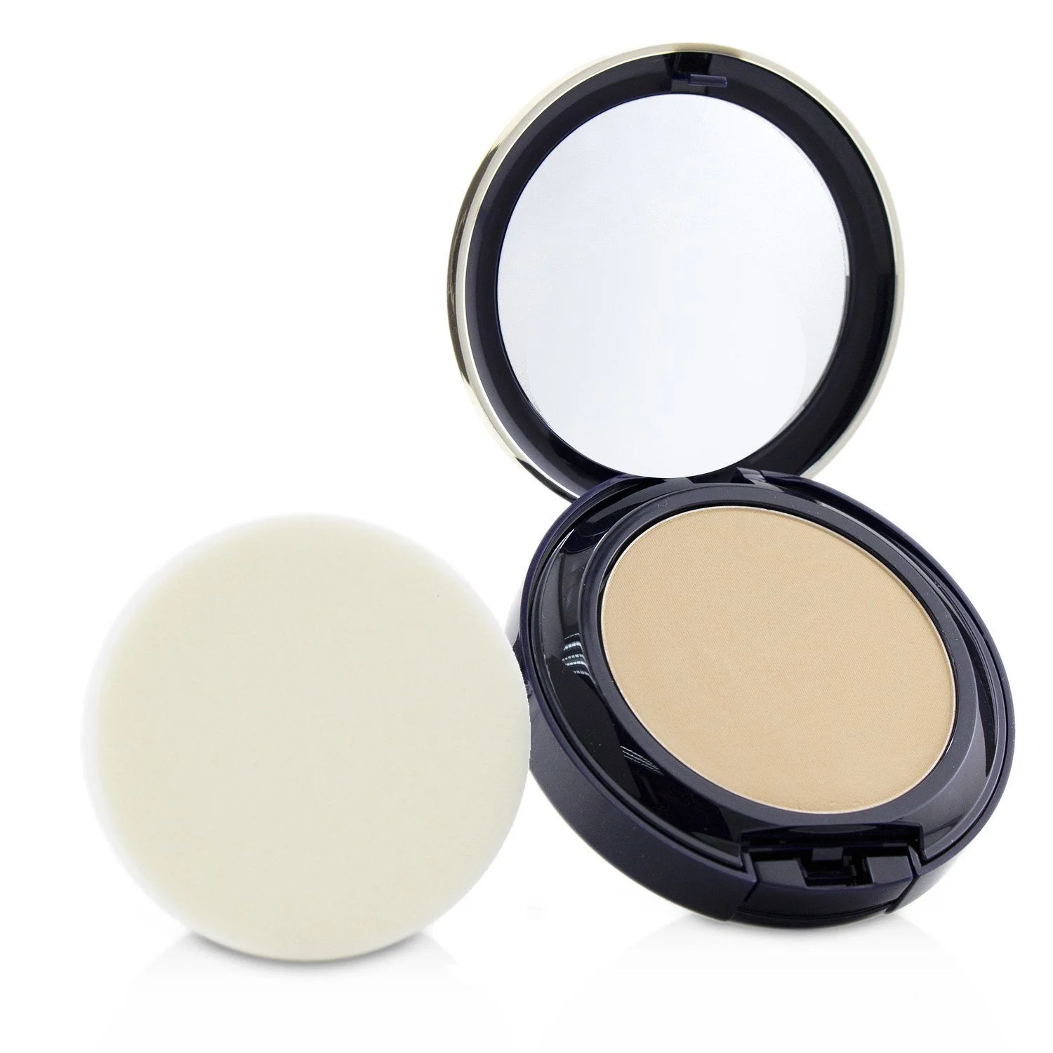 A close-up studio shot of a compact powder foundation and its applicator on a white background. The compact is open, revealing a mirror and the foundation inside. The applicator, a round, flat sponge, sits to the left of the compact.