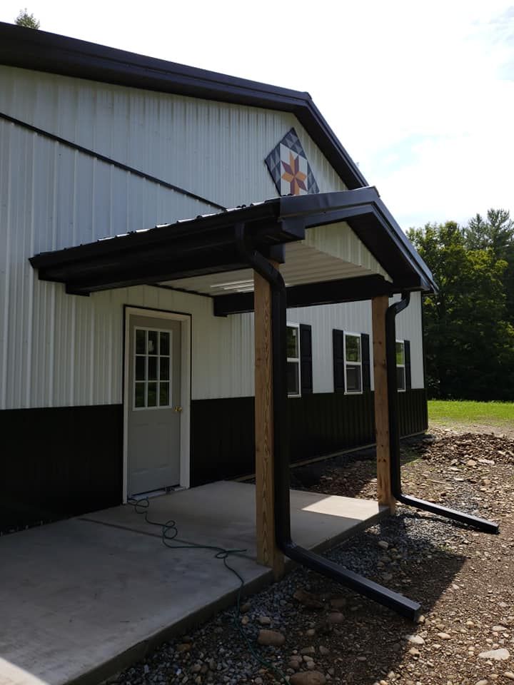 A metal building with white siding and black trim, featuring a covered porch supported by wooden posts, a single entry door, and installed gutter system for effective rainwater management.