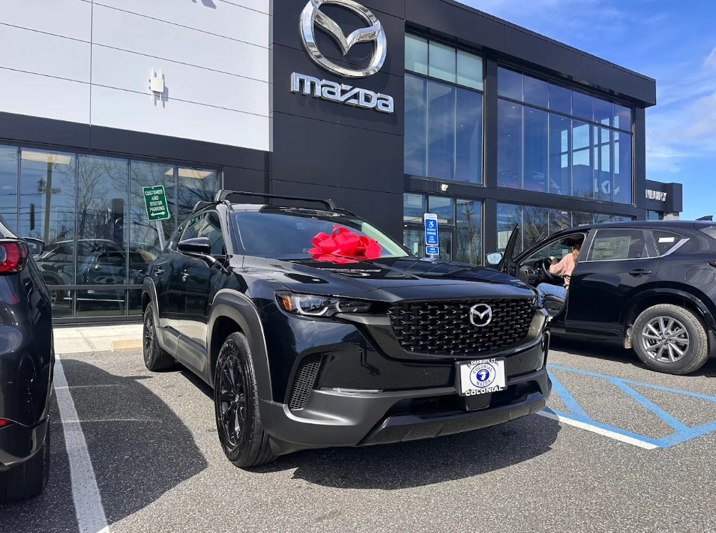 Black Mazda CX-50 SUV with a red bow parked in front of Colonial Mazda dealership in Danbury, CT