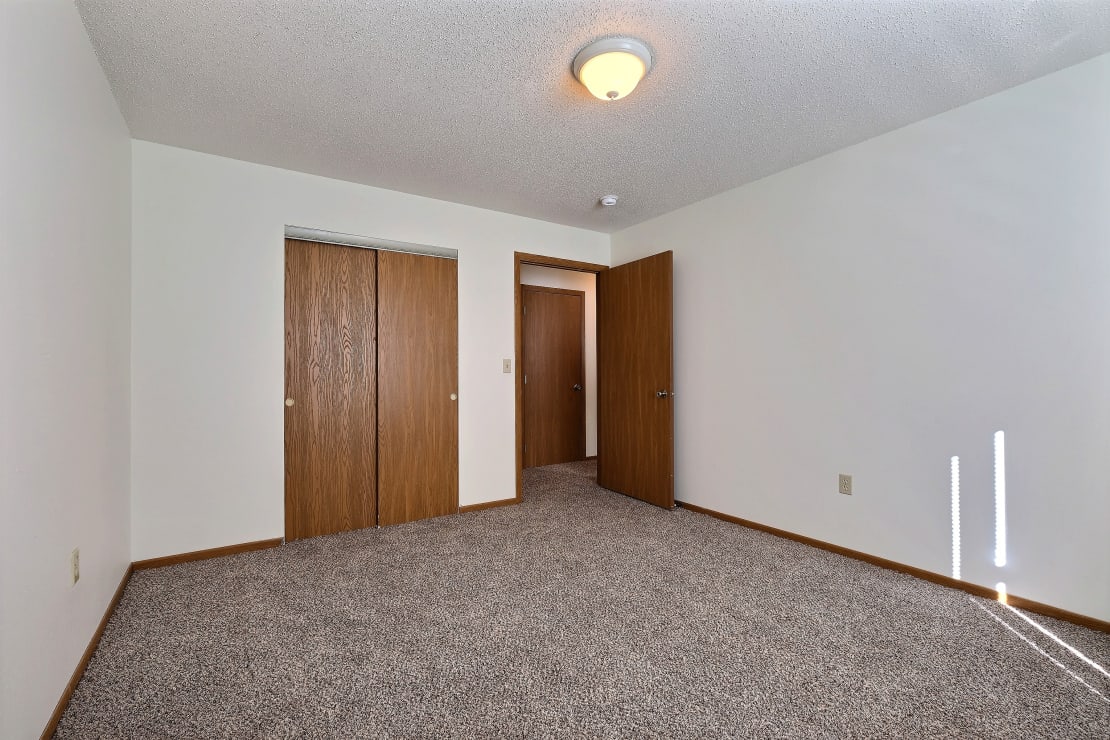 an empty living room with carpet and two doors to a closet