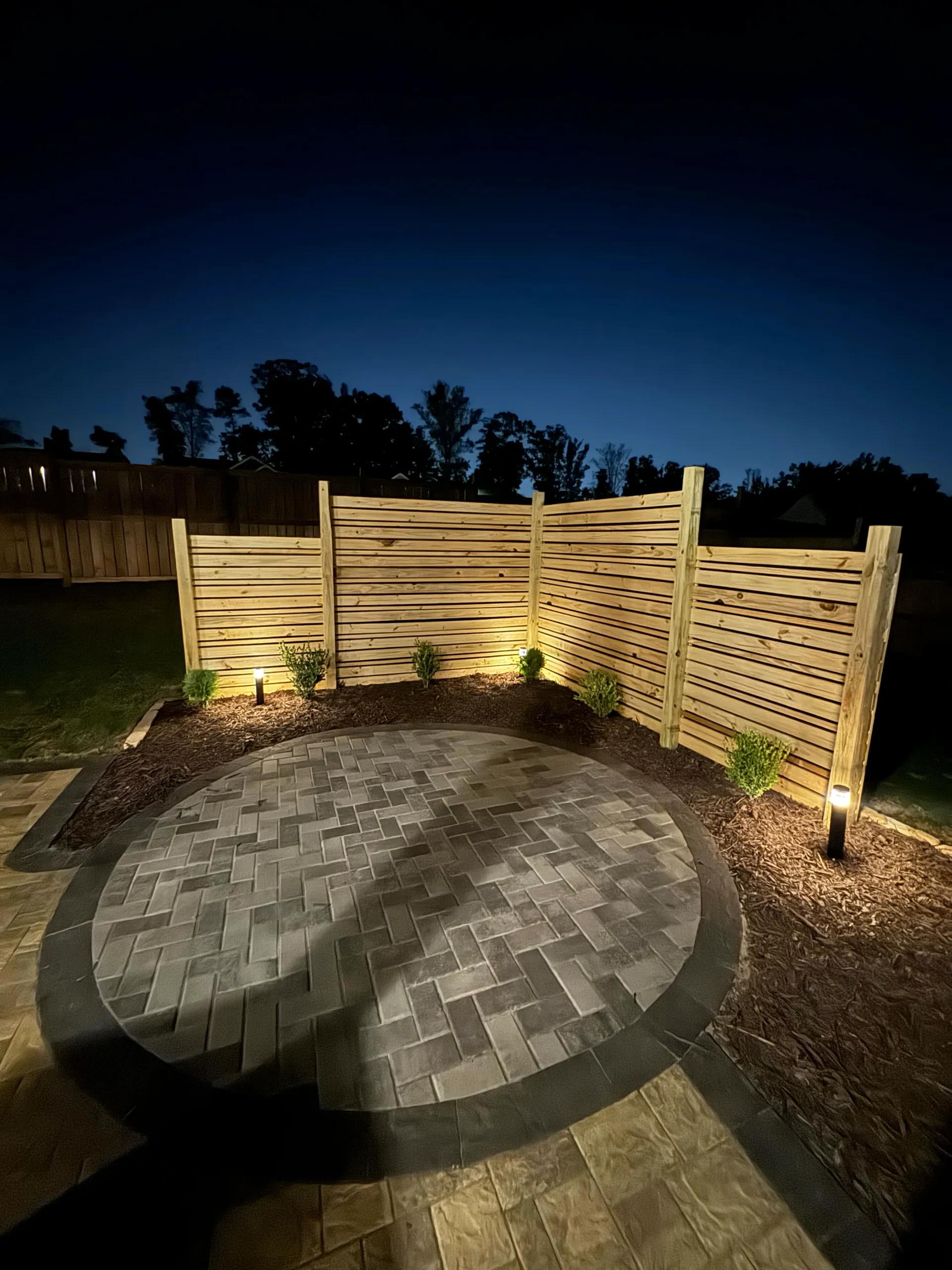 This evening shot showcases Zamora Design and Build's ability to create stylish and functional outdoor spaces, highlighting their expertise in paver installation, contemporary fencing, and effective lighting design.