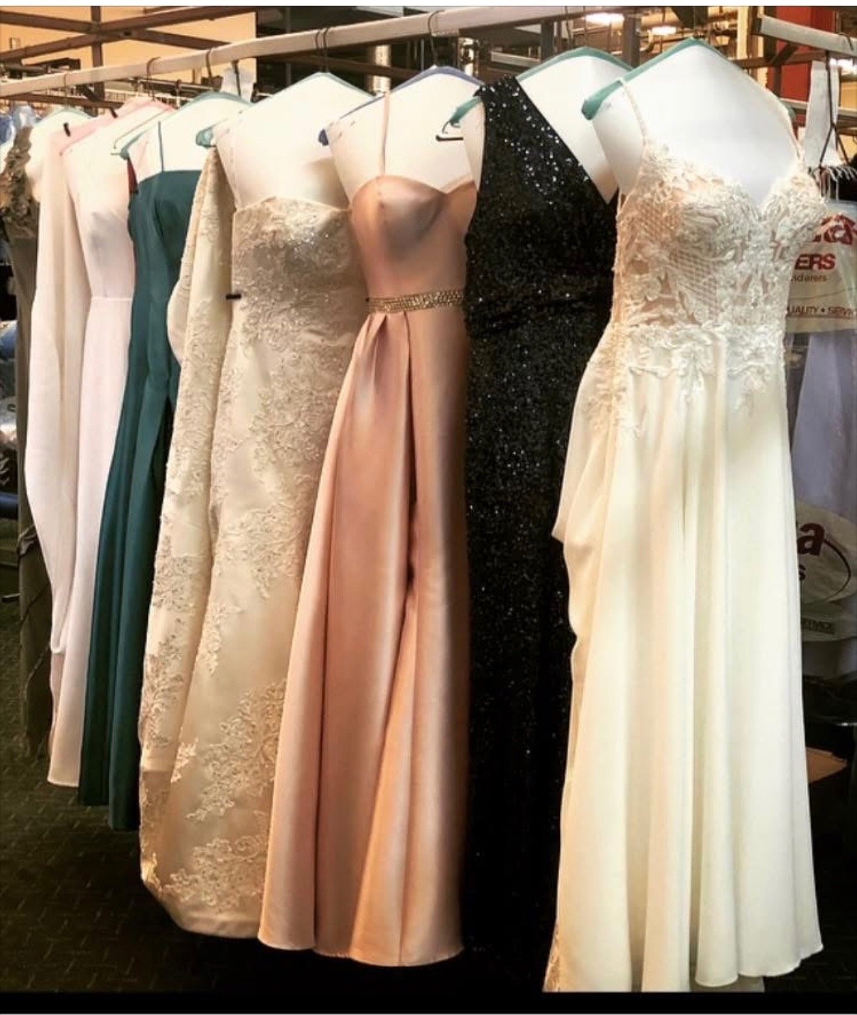 A colorful row of elegant bridesmaids and formal gowns&mdash;featuring satin, lace, and sequins&mdash;hanging on display racks after professional cleaning at Plaza Cleaners.