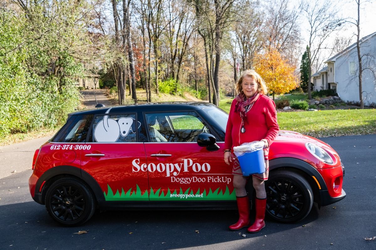 ScoopyPoo branded vehicle parked outside a residential property beside a team member holding collection bucket, promoting dependable dog waste removal services with professional mobile branding and neighborhood convenience.