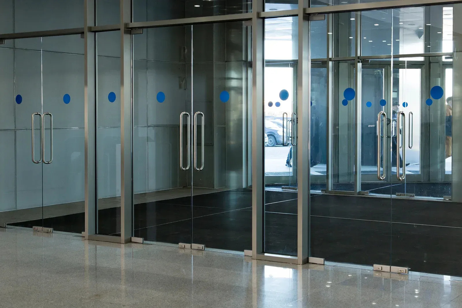 Interior commercial lobby features multiple full-height glass doors and partitions with metal frames 