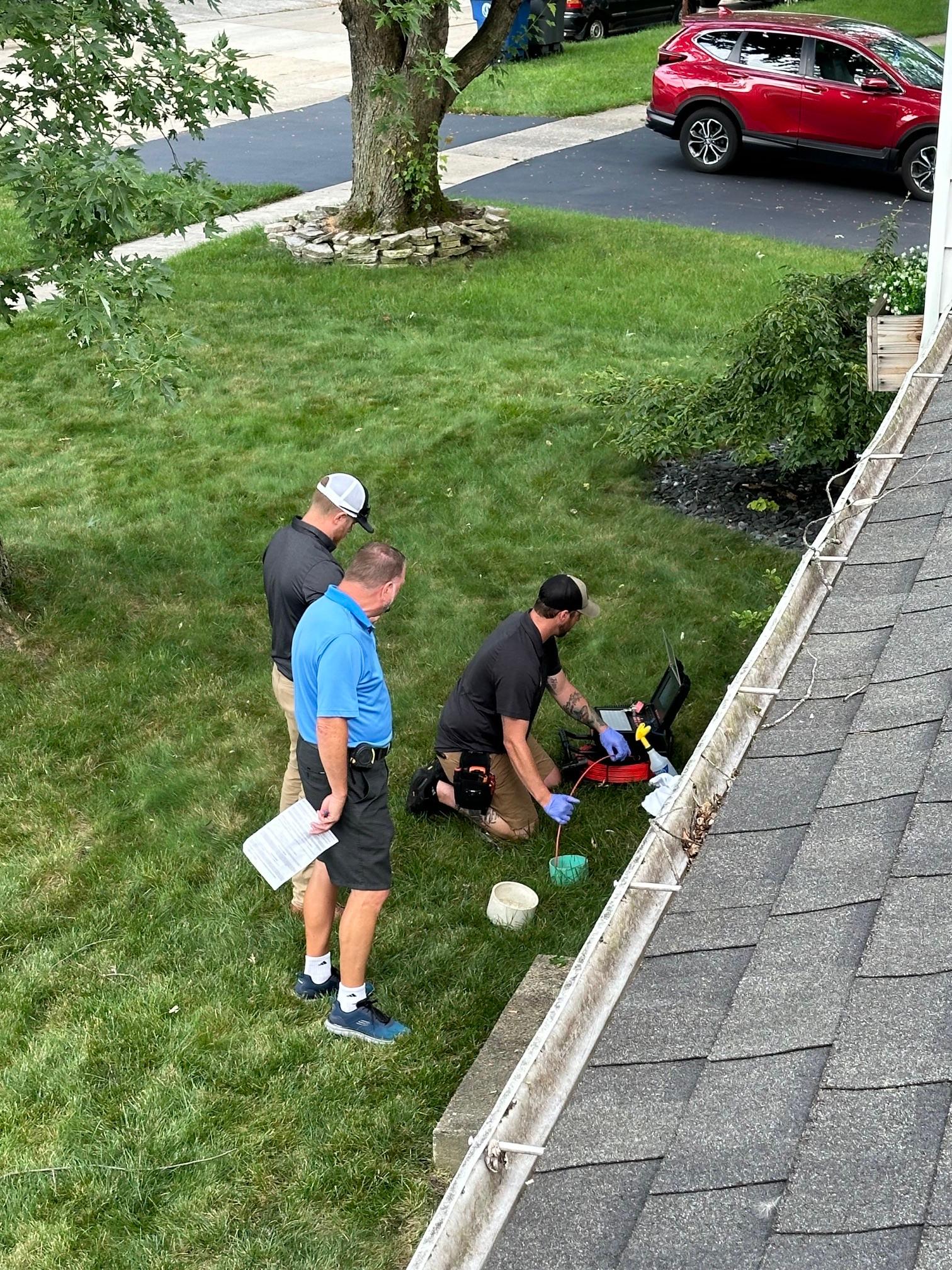 High-angle view of three home inspectors using portable camera equipment to conduct a sewer scope inspection on a lawn.