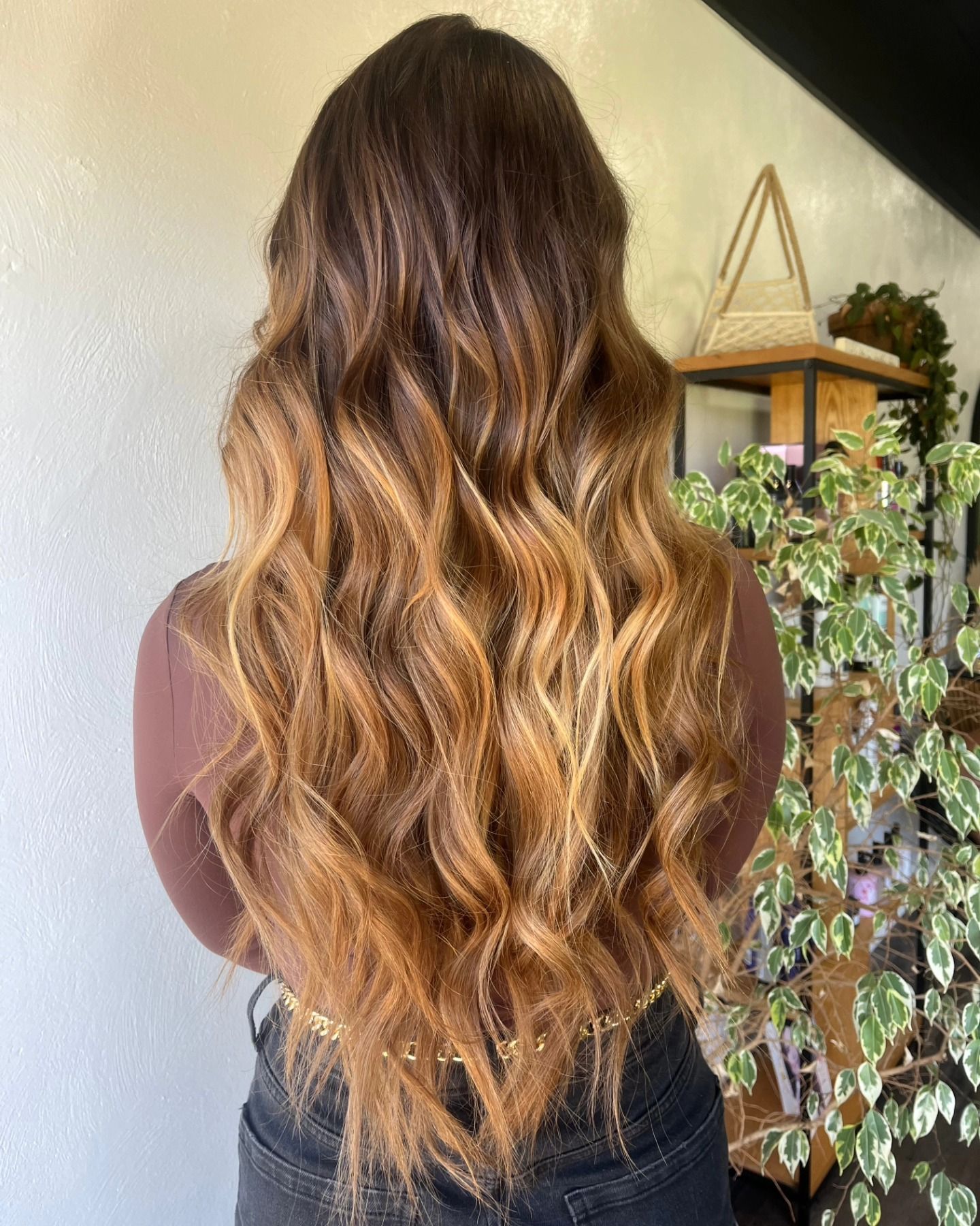 Back view of woman with long wavy brown hair featuring warm caramel balayage highlights styled in loose waves.