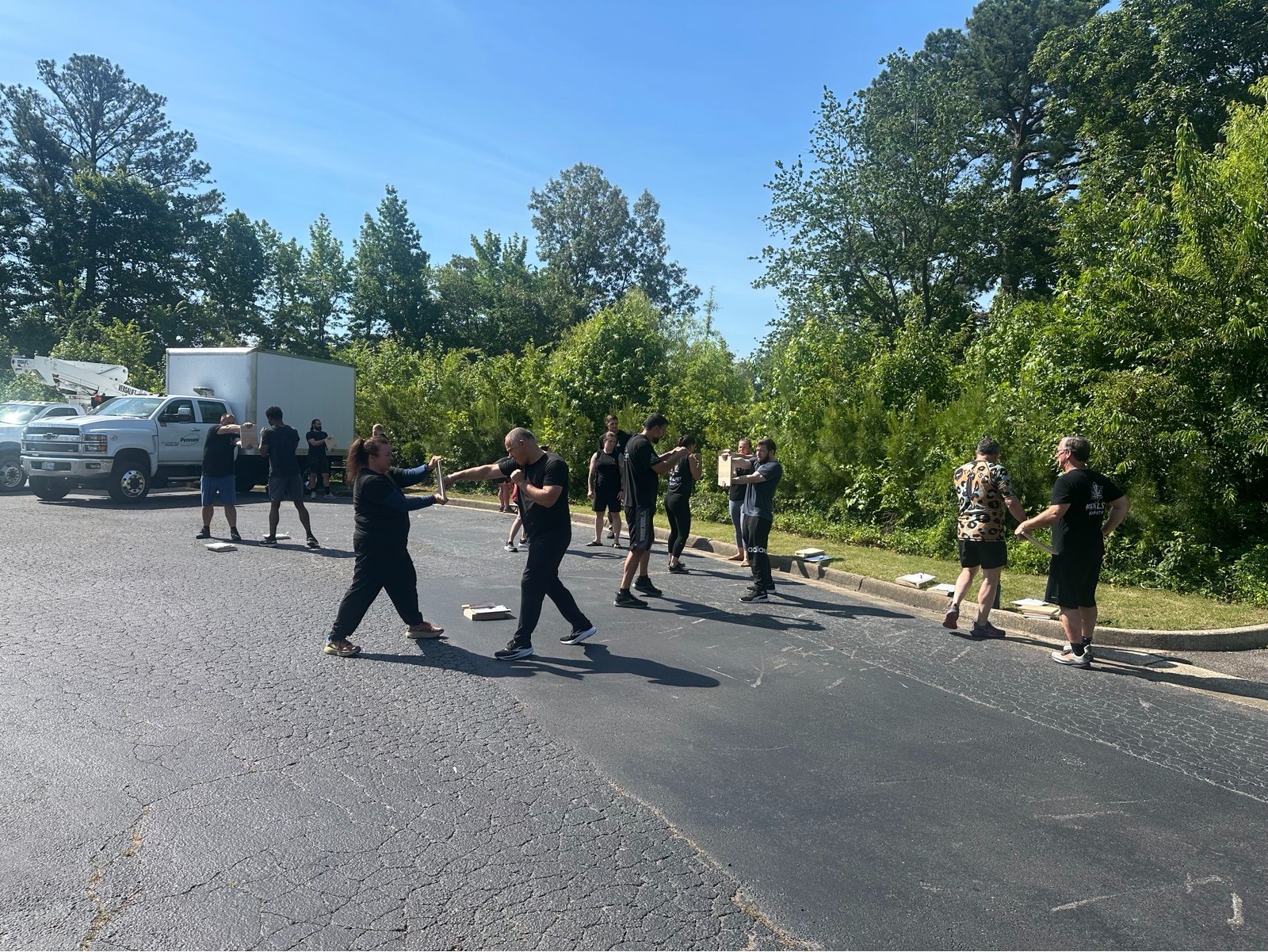 Adult students running paired striking drills outdoors during a warm-weather class.