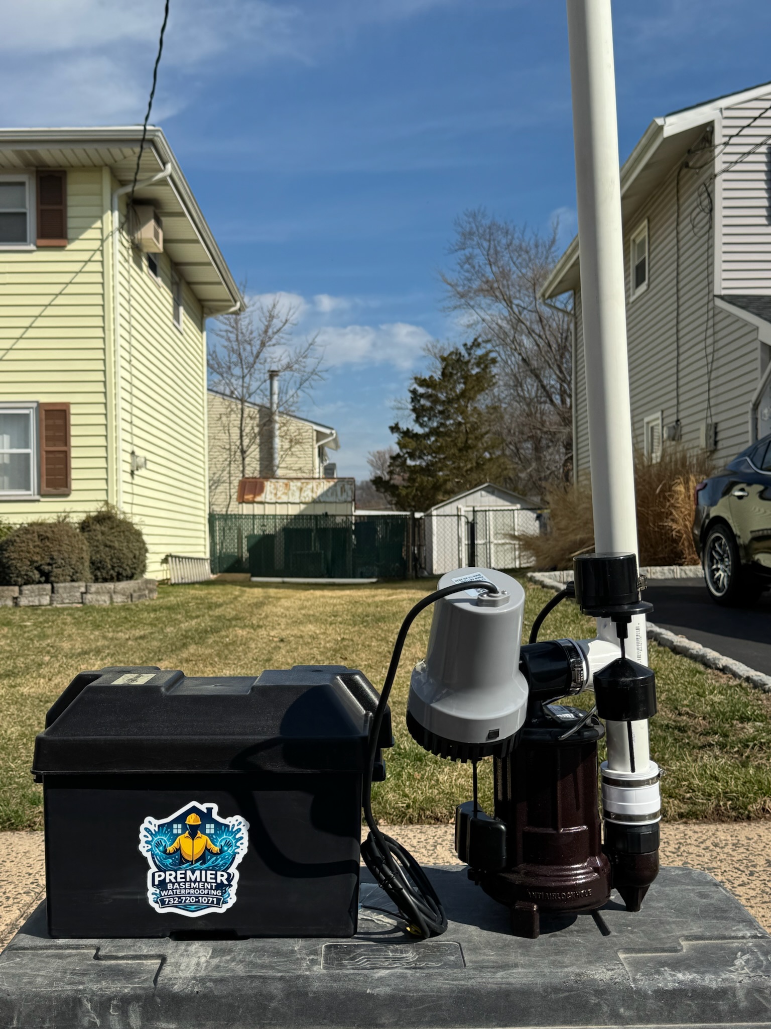 Photo showing waterproofing tools, pump equipment, and a branded Premier Basement Waterproofing case outside a home during a service visit.