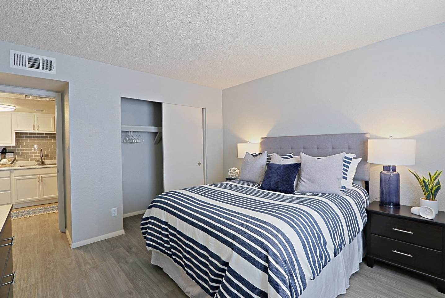 Cozy Bedroom with Stripped Bedding and Plank Flooring with View into Kitchen Area