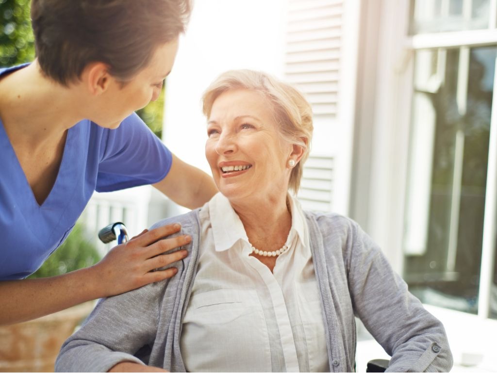 A caregiver warmly interacting with and supporting a smiling senior woman at home, showcasing compassionate companionship and personalized in-home care.