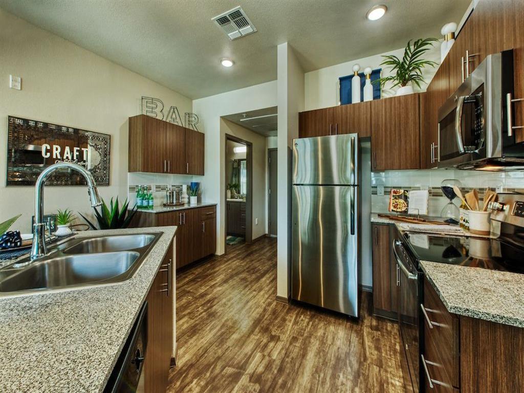 A kitchen with stainless steel double sink and stainless steel refrigerator. Beautiful modern cabinets line kitchen walls and surround black range.