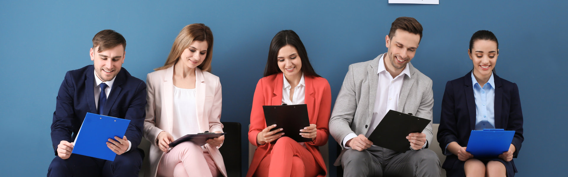 Five diverse individuals in professional attire are seated in a row against a blue background, each  