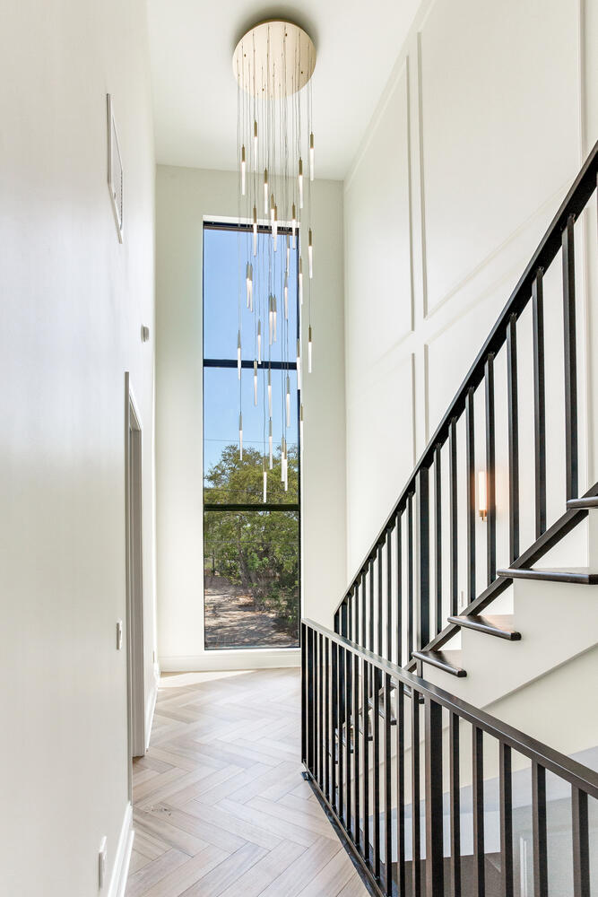 Bright interior stairway with black metal railing, tall windows, natural light, and a clean modern custom home design.