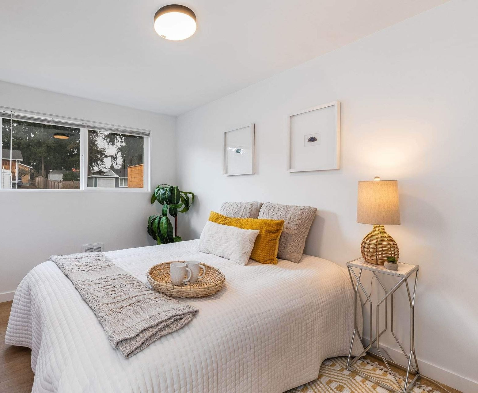 A bright bedroom features a neatly made white bed, textured neutral bedding, mustard accent pillows, 