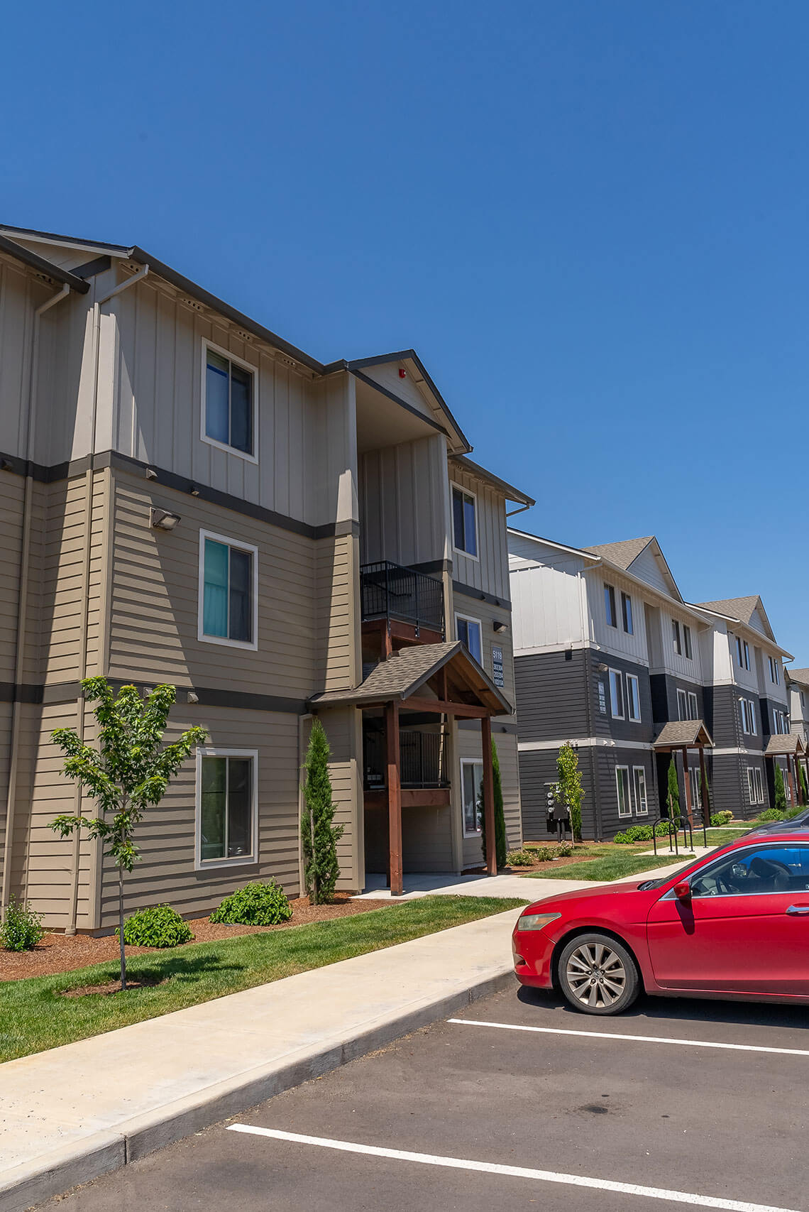A red car is parked in a parking lot in front of a building.