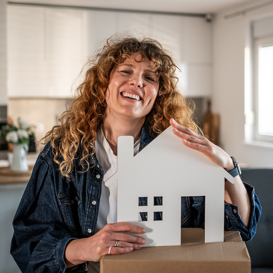 A woman smiling and holding a cutout of a house