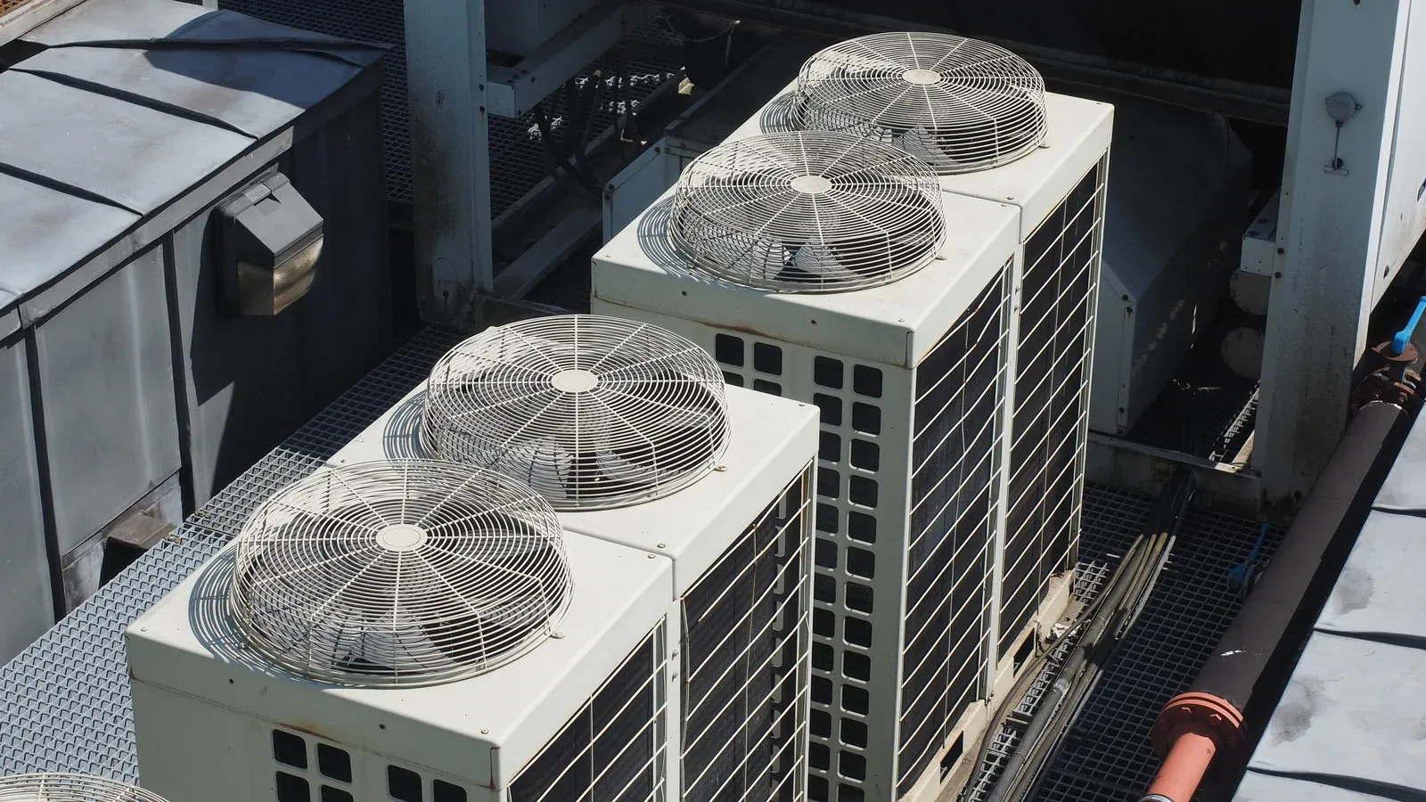 A high-angle shot displaying four large commercial HVAC condenser units on a rooftop. The white systems feature dual top-mounted fans with circular wire guards and black side ventilation panels.