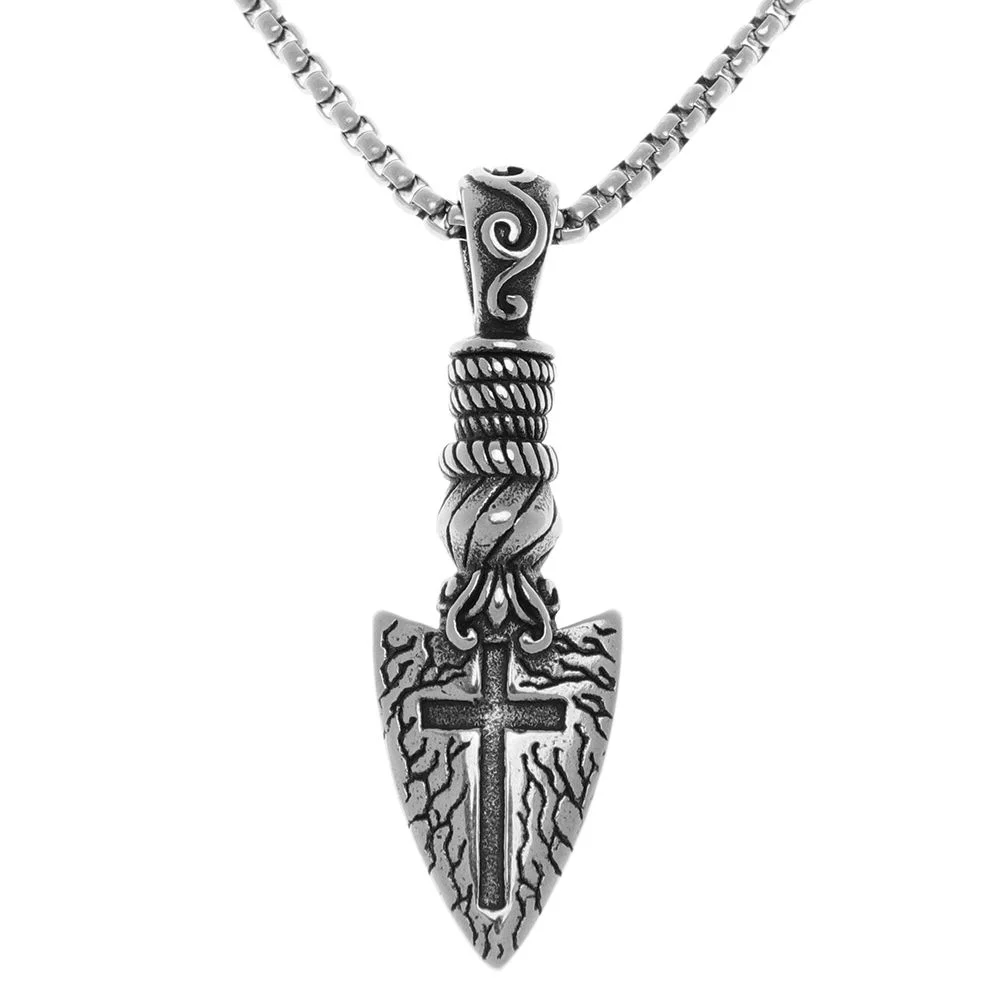A close-up, studio shot of a silver arrowhead pendant on a silver chain. The arrowhead has intricate detailing, including a cross symbol at its center and a textured, bark-like pattern on its surface. The bail of the pendant is designed to resemble a wrapped rope, and the top of the bail features a swirling, decorative element. The chain is a sturdy, box-link style. The background is pure white, isolating the jewelry.