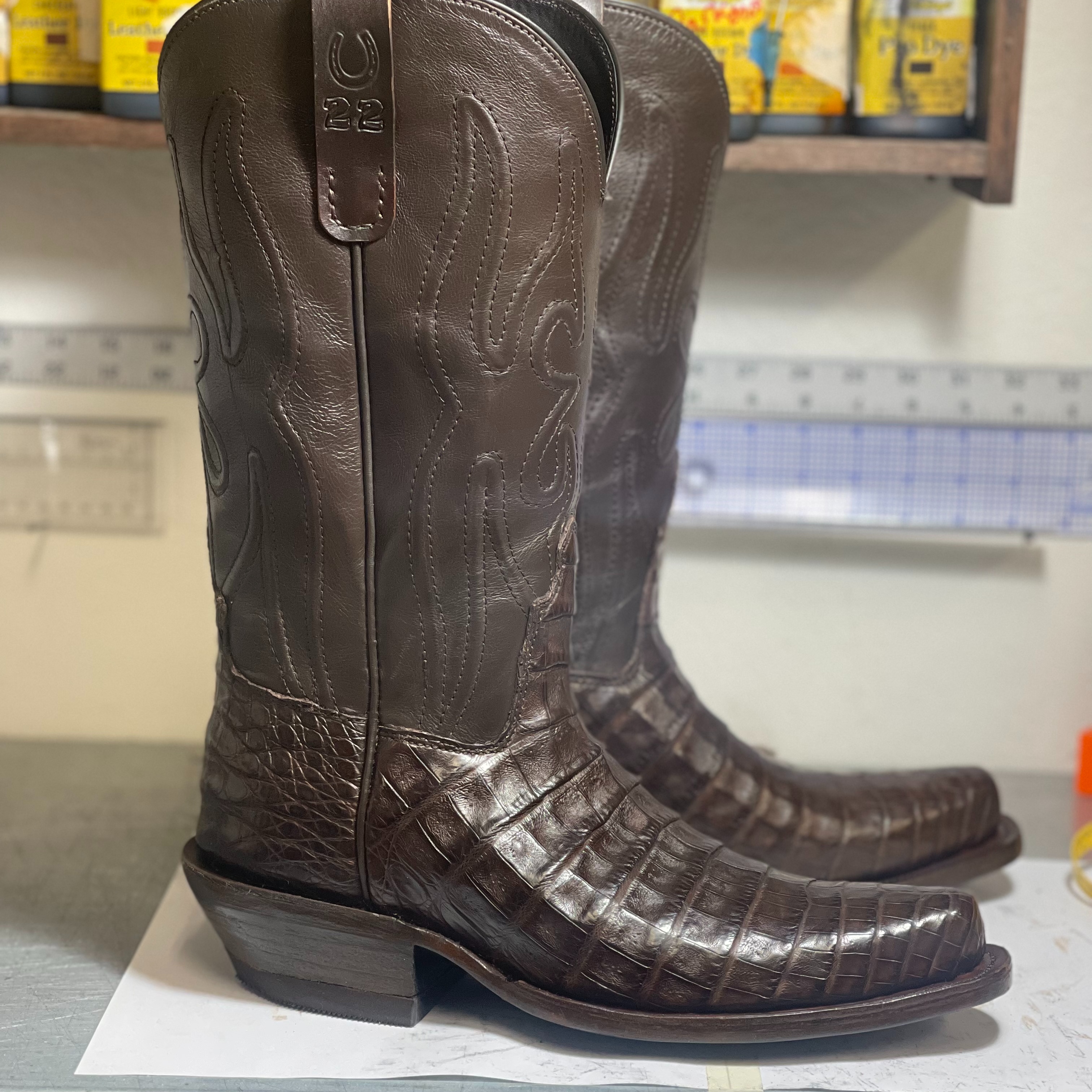 A pair of brown custom cowboy boots featuring reptile-textured leather, matching shafts, and square  