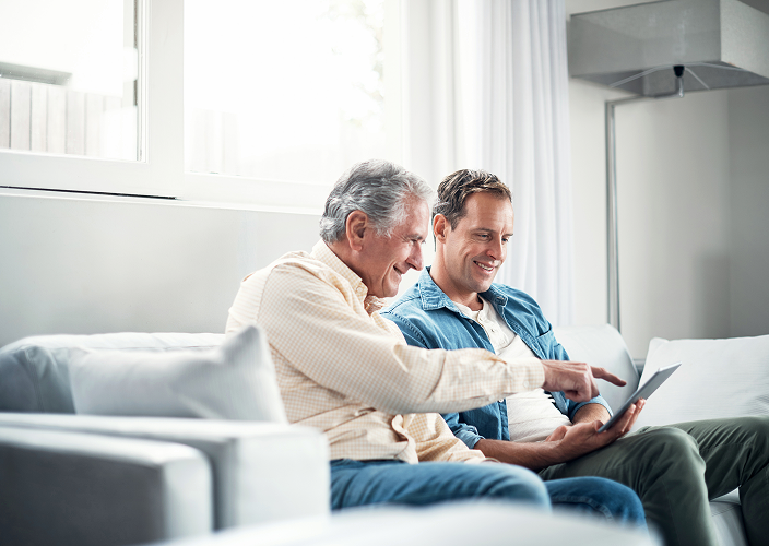 An elderly father and his adult son looking at a tablet together.