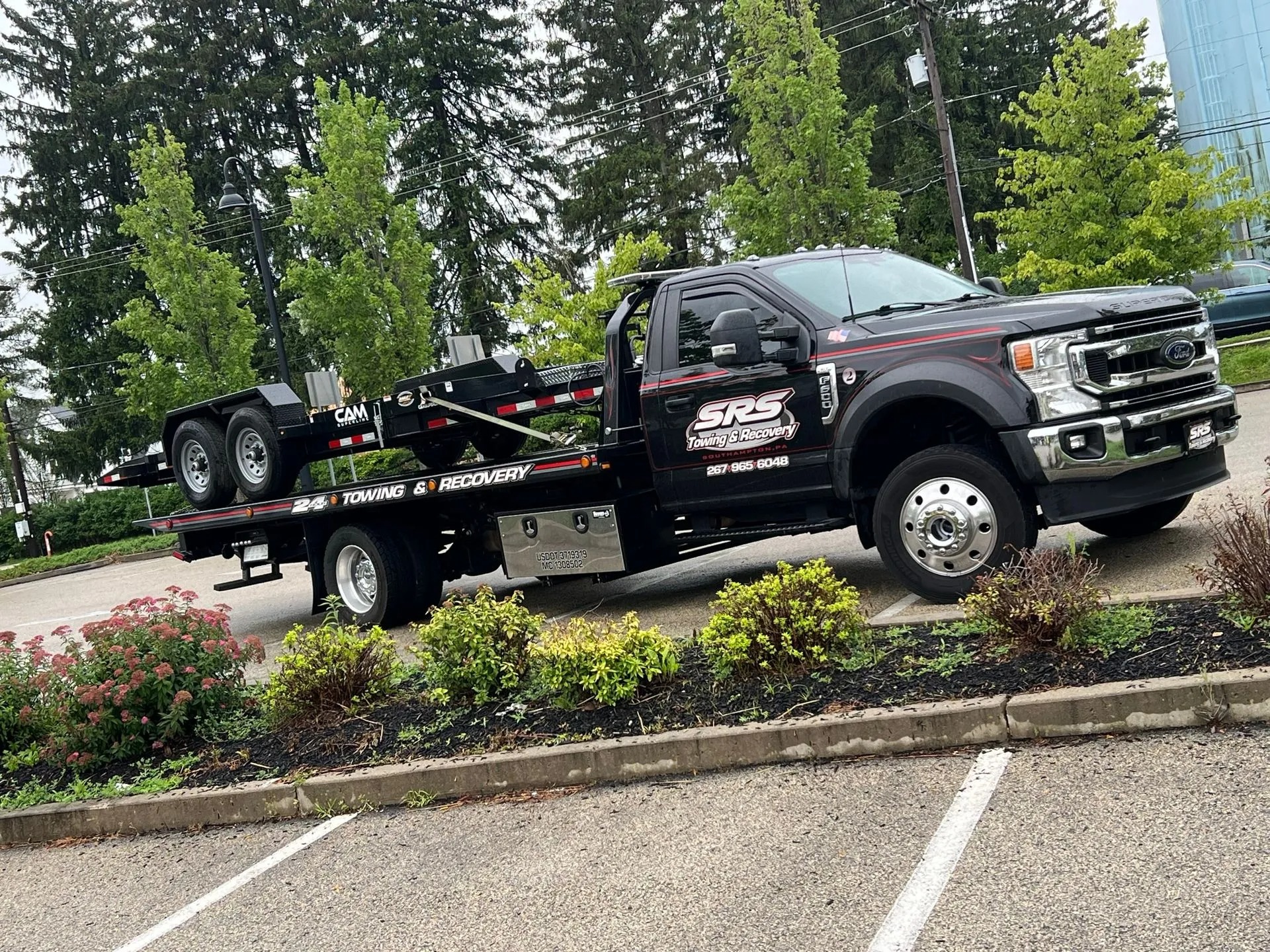 A Ford heavy-duty tow truck from SRS Towing & Recovery, loaded with a black CAM Superline dual-axle equipment trailer.