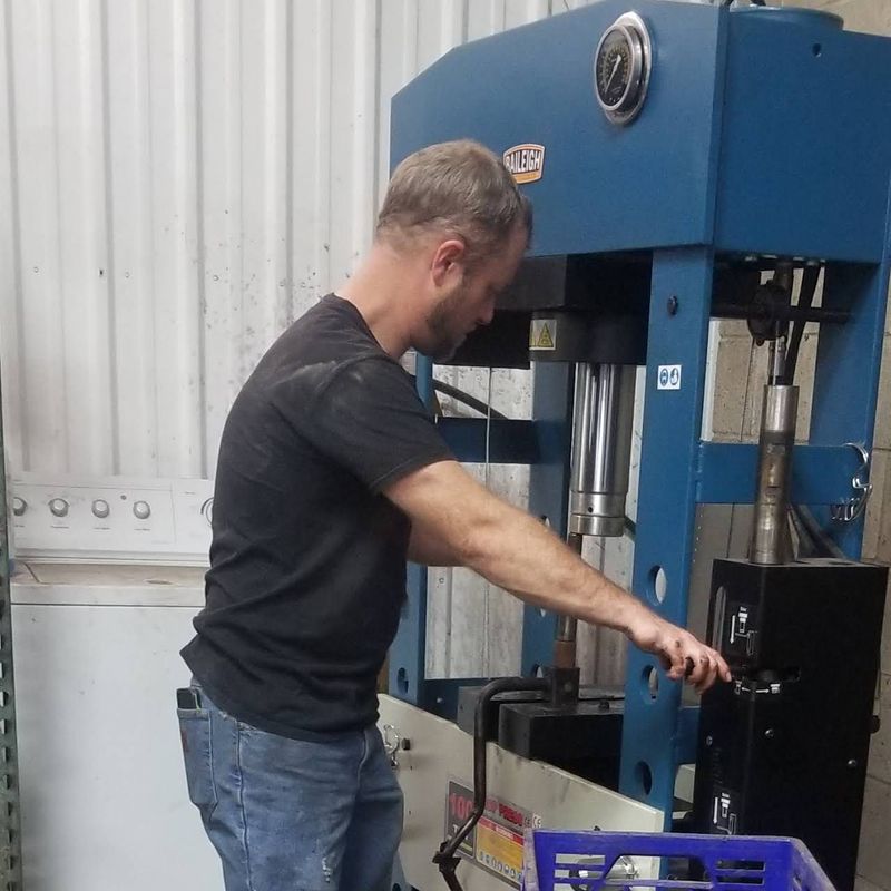 A technician in a black t-shirt operates a large blue Baileigh industrial hydraulic press in a works 