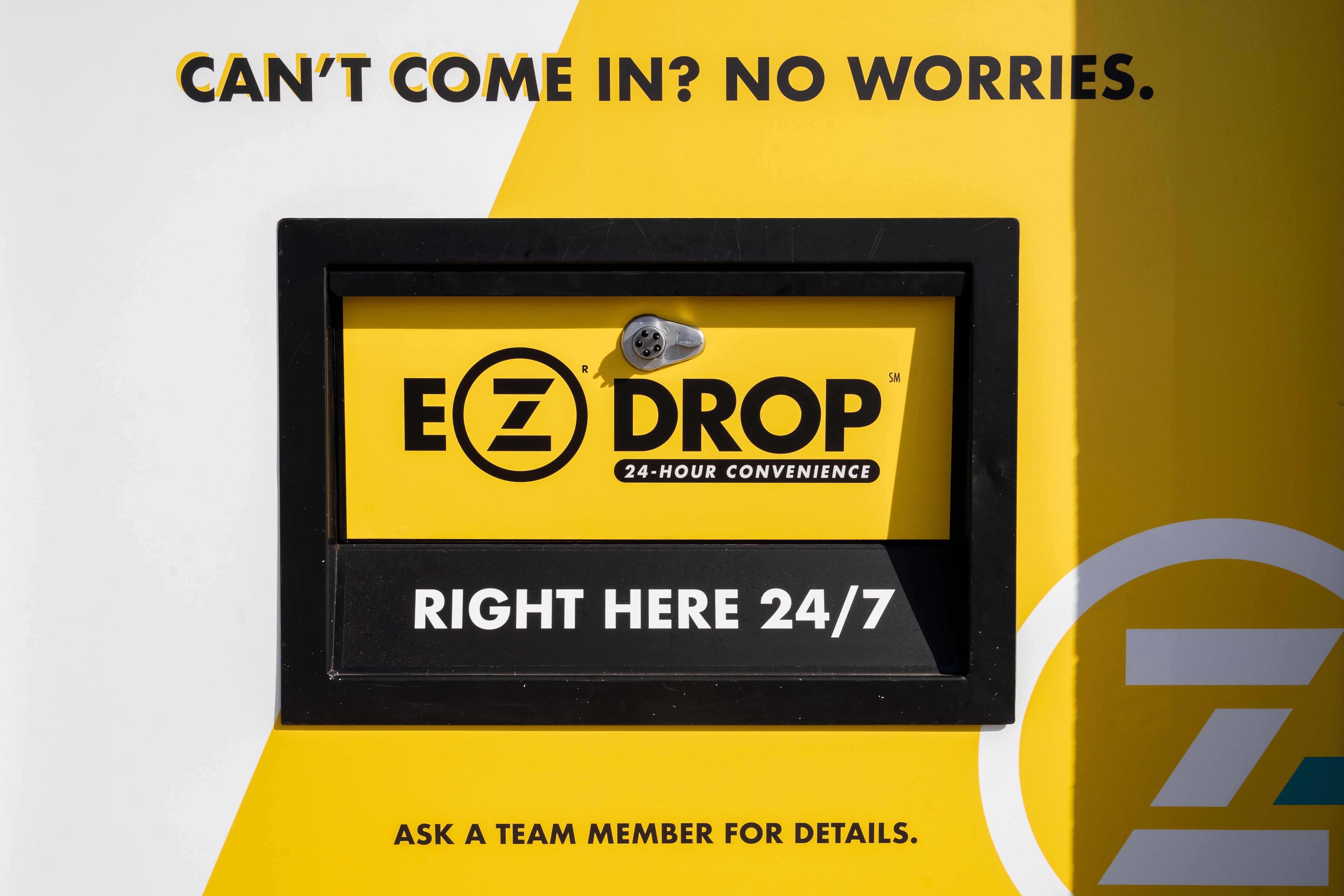 Front view of ZIPS Cleaners EZ Drop box in iconic Gold and black. Text on box explains how easy and convenient it is to use our ZIPS Cleaners EZ Drop box. Can’t come in? No worries. EZ Drop 24-Hour Convenience. Right here 24/7. Ask a Team Member for details. It is that EZ.