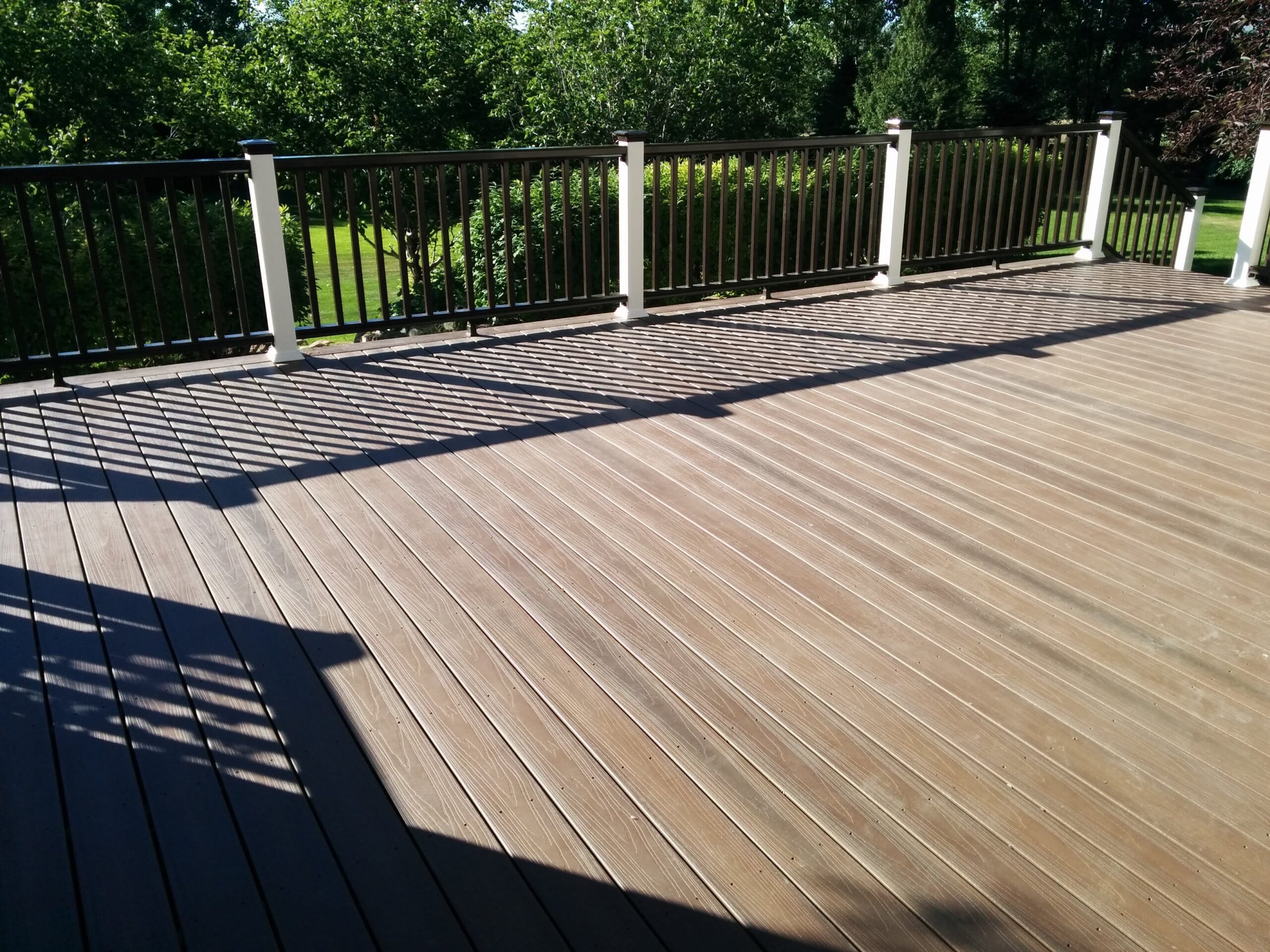 Expand your outdoor living possibilities with this custom deck by DeckPro LLC, which combines rustic elements with modern materials. We installed low-maintenance composite decking in a warm brown tone and paired it with a unique railing system that features natural wood posts and integrated wire mesh infill panels. For the ultimate in functional design, we included extensive built-in L-shaped bench seating, creating a cozy and inviting perimeter perfect for taking in scenic views.