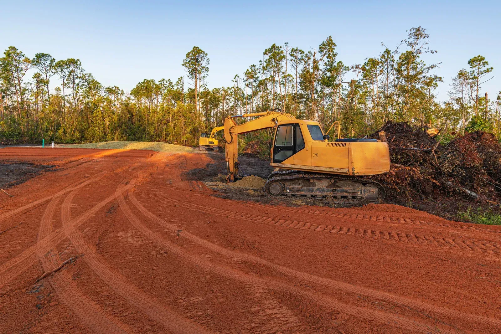 Heavy excavator equipment performing large-scale land clearing and grading services on a construction development site. The prepared terrain demonstrates professional earthmoving, soil leveling, excavation, and site preparation work for future residential or commercial building projects.