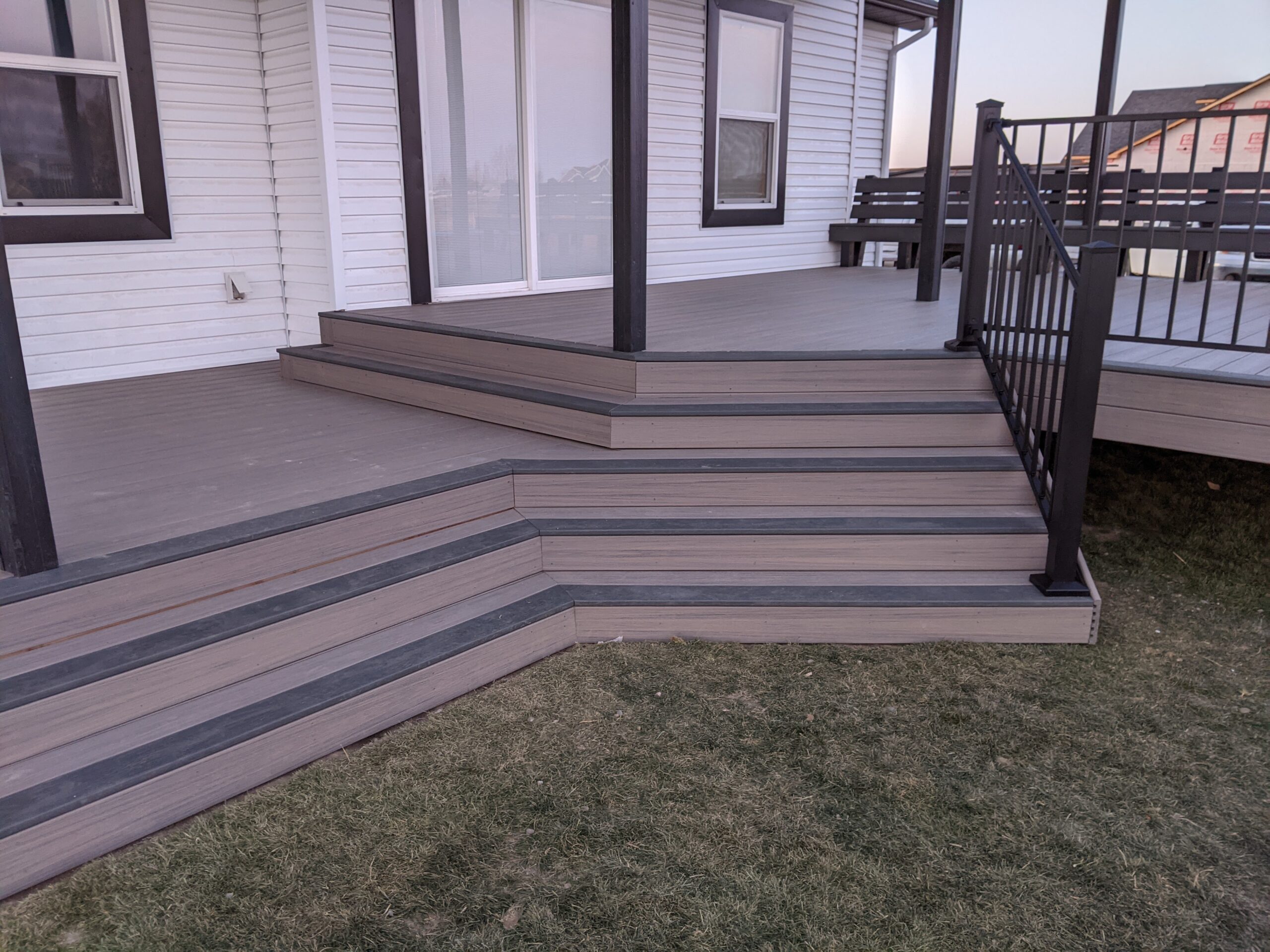 Make a grand entrance to your backyard with custom craftsmanship from DeckPro LLC. This grey composite deck features elegant, wide cascading stairs highlighted by dark "picture framing" borders and sleek black metal railing, perfect for Southeast Idaho homes.