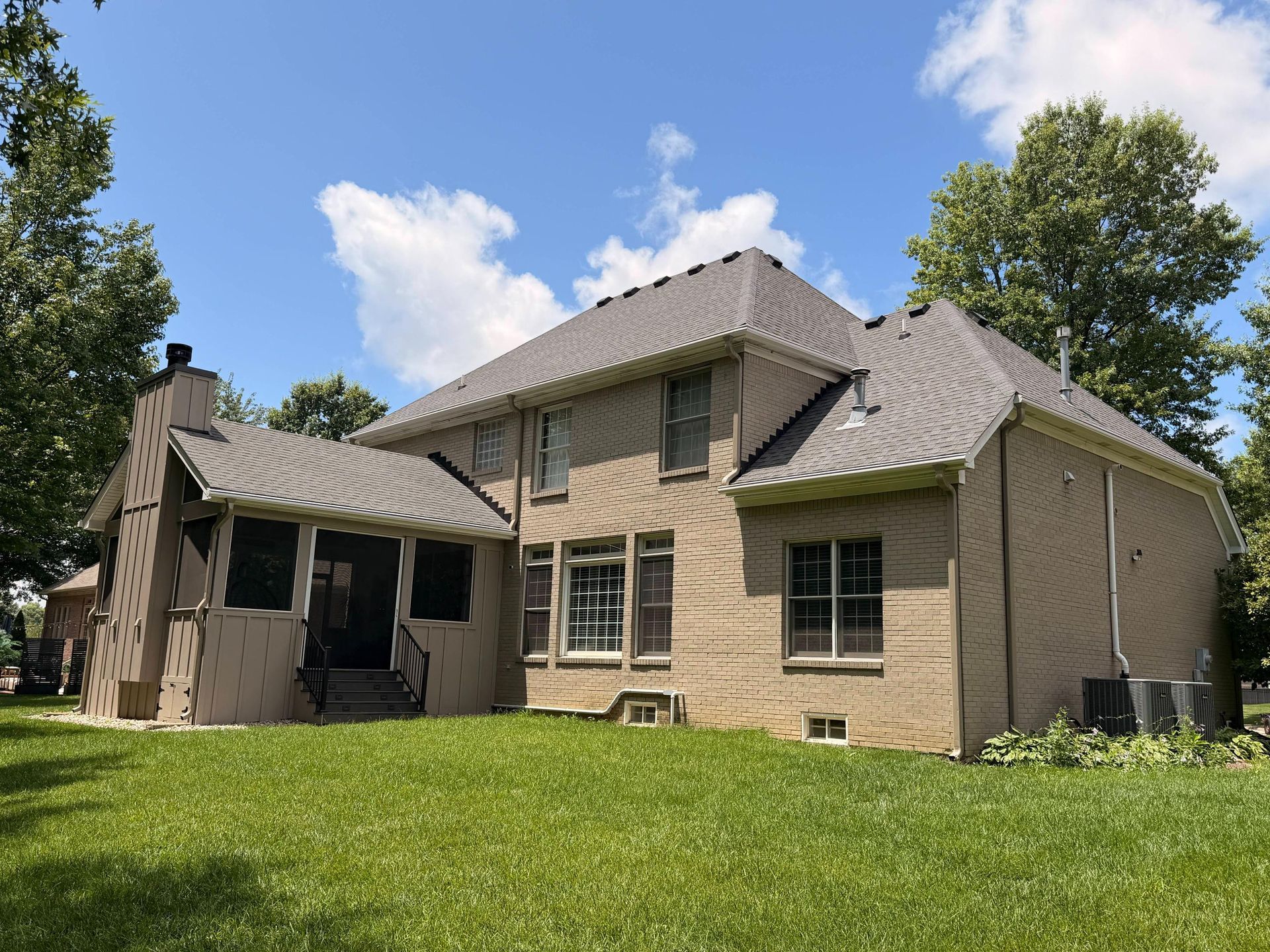 Rear view of a two-story brick home featuring a professionally installed gray shingle roofing system 