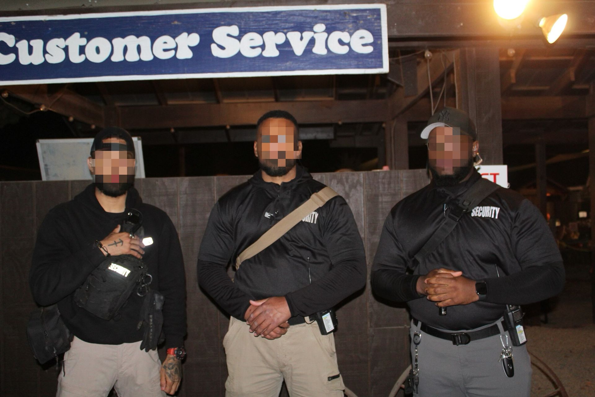 Three security personnel stand in front of a "Customer Service" sign at night, wearing black uniforms and tactical gear.