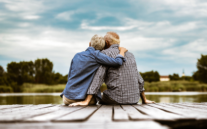 An elderly couple sitting on a dock and looking out at the water.