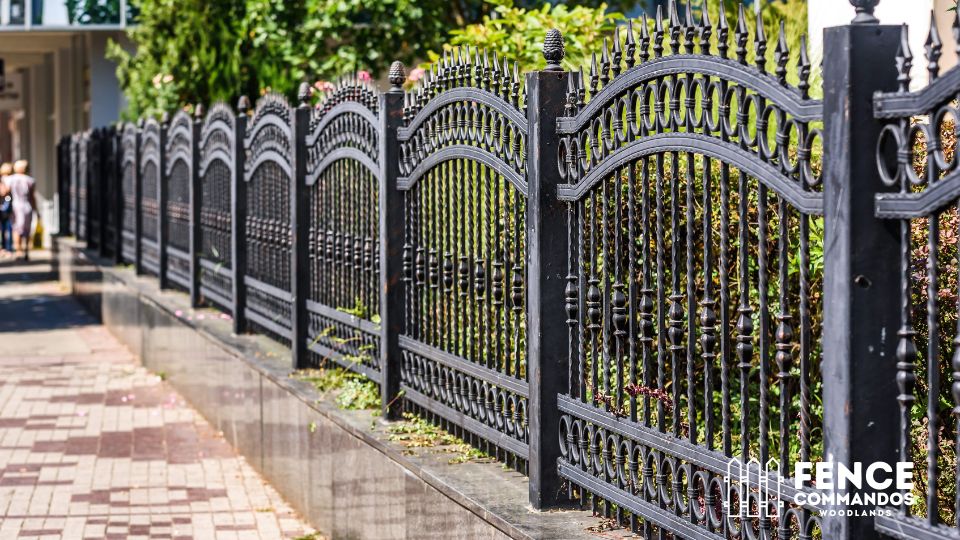 Ornamental black steel fence with decorative arches and detailed metalwork along a residential sidewalk.