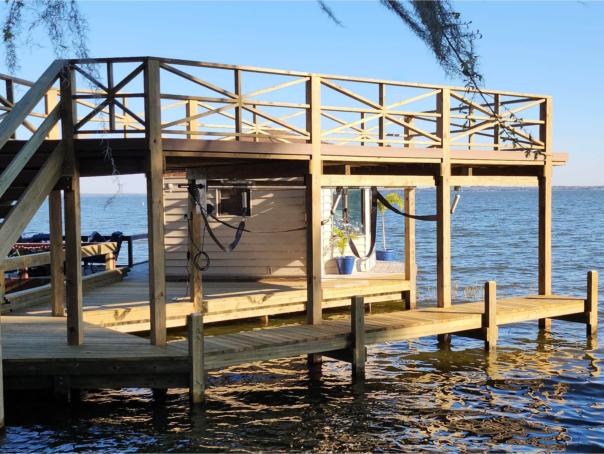 A wooden dock with a two-level structure extends over calm lake waters. The sun casts soft shadows, creating a serene and peaceful atmosphere.