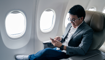 A man in a first-class airplane seat, scrolling on his phone.
